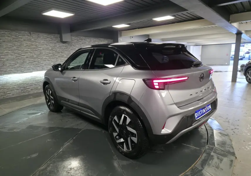 Opel Mokka-e gris 3/4 arrière droit, toit noir, jantes alliage diamantées, feux arrière LED allumés.