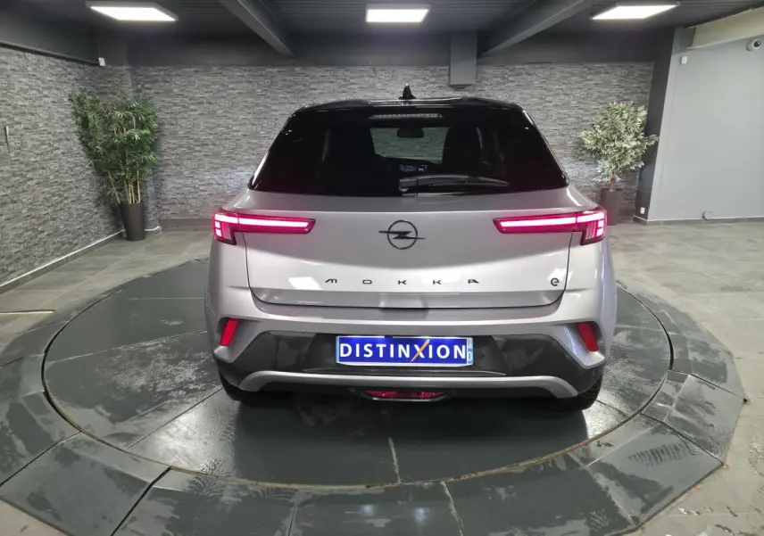 Vue arrière d'un Opel Mokka-e gris 2025 avec feux LED allumés et toit noir dans un showroom.