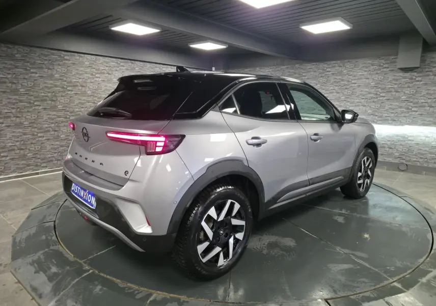 Opel Mokka-e gris 3/4 arrière droit, toit noir, jantes alliage diamantées 17 pouces, feux arrière LED allumés.