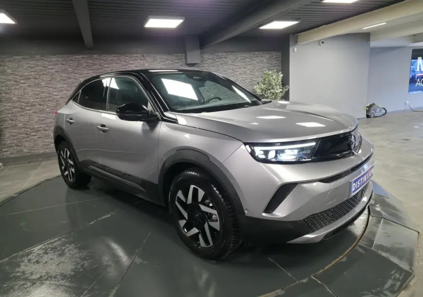 Opel Mokka-e gris 3/4 avant droit avec jantes alliage diamantées et toit noir en intérieur showroom.