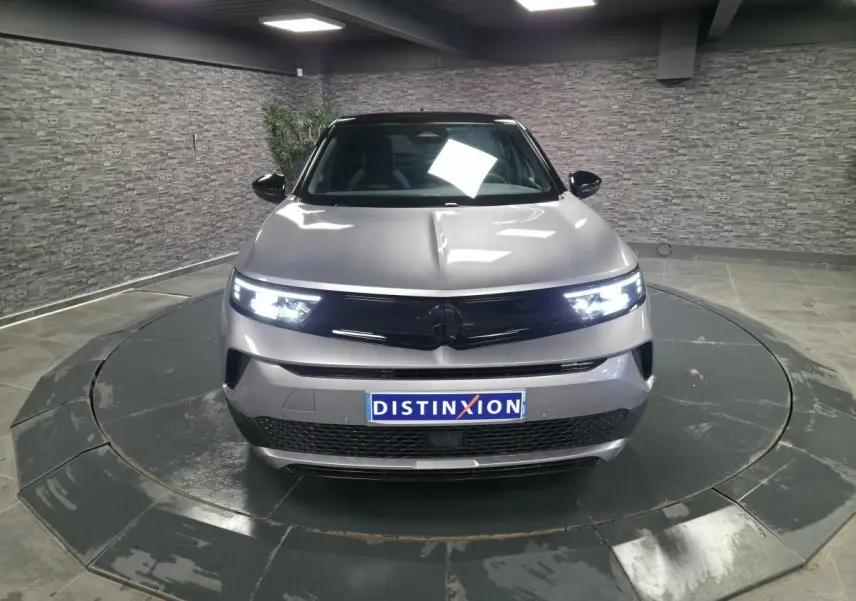 Opel Mokka-e gris vue de face en intérieur, avec phares Matrix LED allumés et calandre noire brillante.