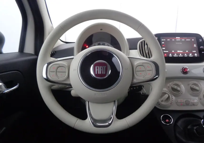 Vue rapprochée du volant beige clair de la Fiat 500 1.0 Hybrid 2023 avec tableau de bord et écran tactile visible.