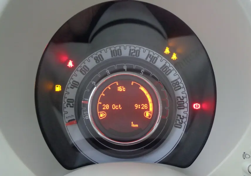 Vue rapprochée du tableau de bord numérique de la FIAT 500 blanc gelato avec affichage des voyants d'alerte allumés.