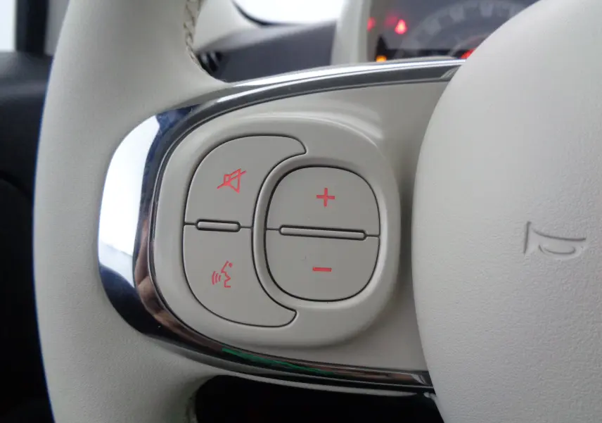 Gros plan sur les commandes de volume et de coupure du son sur le volant blanc de la FIAT 500 2023 hybride.