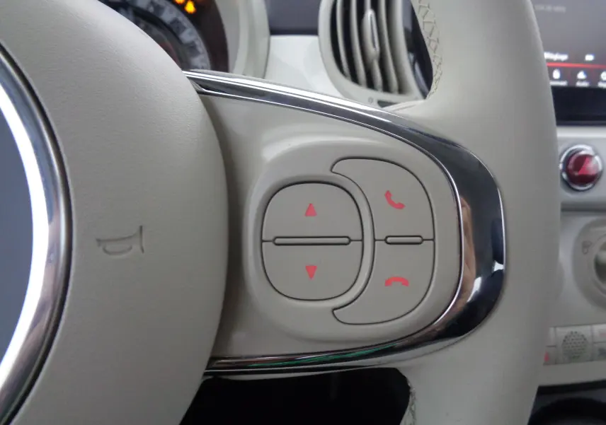 Gros plan sur les commandes de téléphone et volume à droite du volant beige de la Fiat 500 blanc gelato 2023.