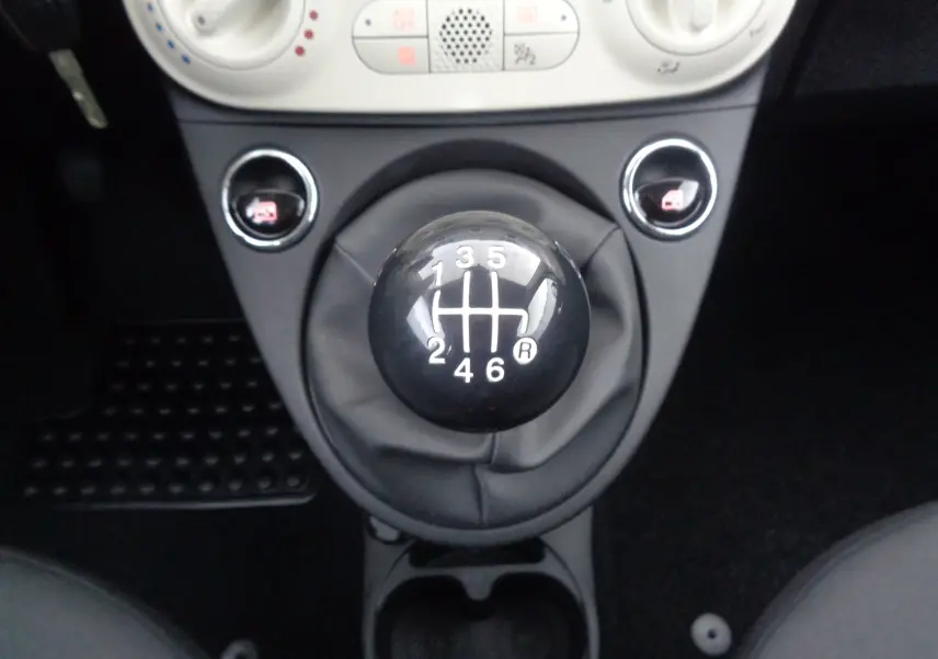 Le levier de vitesses manuel noir de la FIAT 500 blanc gelato, vu de dessus au centre de la console.