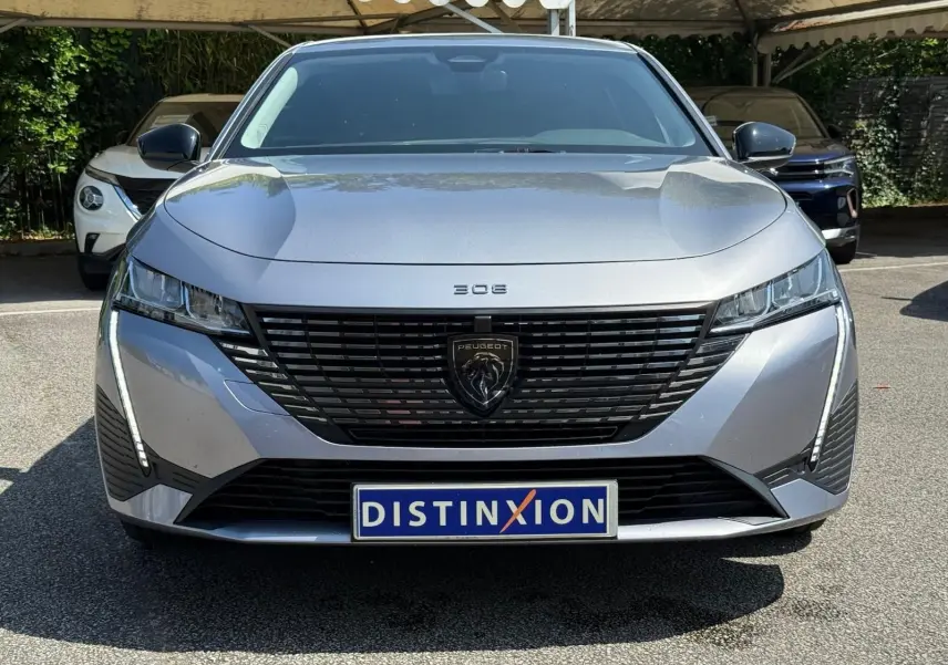 Vue frontale d'une Peugeot 308 2024 gris Artense avec calandre noire et feux LED en forme de griffes.