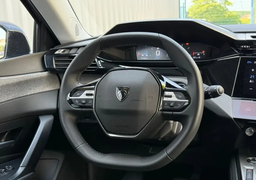 Vue rapprochée du volant cuir noir de la Peugeot 308 2024 avec tableau de bord digital et commandes intégrées.