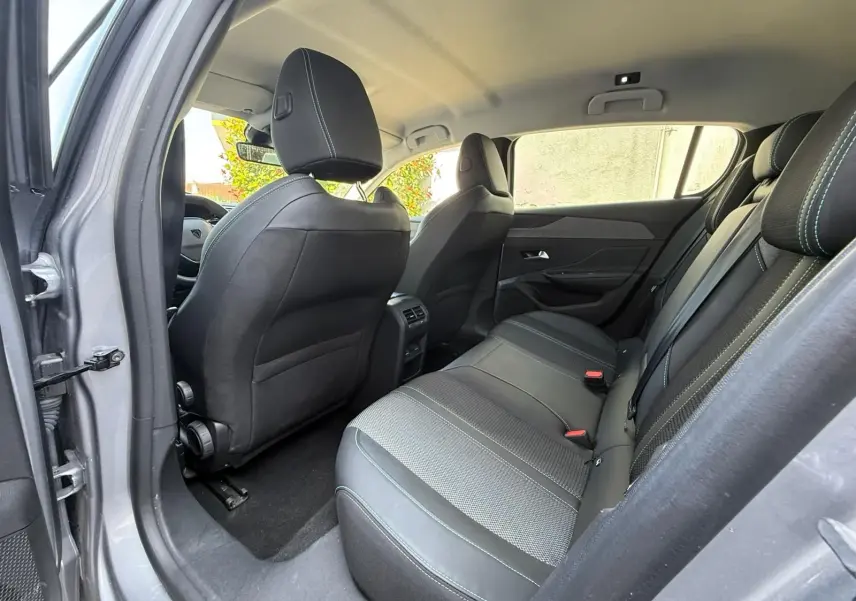 Vue intérieure arrière côté gauche de la Peugeot 308 2024 gris Artense, montrant les sièges arrière en tissu et cuir noir.