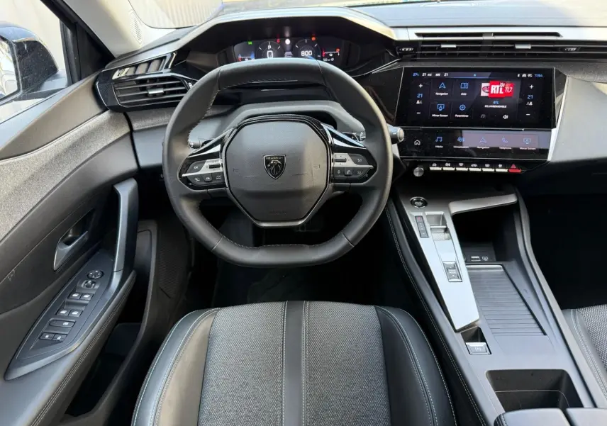 Vue intérieure centrée sur le volant et la console centrale d'une Peugeot 308 2024 avec écran tactile et finitions modernes.