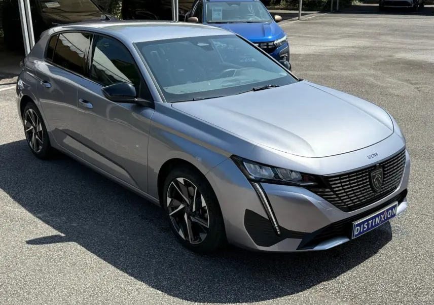 Vue 3/4 avant gauche d'une Peugeot 308 gris Artense 2024 avec calandre noire et phares LED distinctifs.