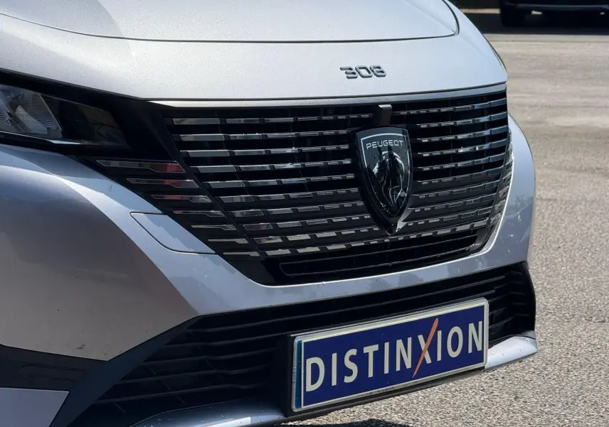 Vue rapprochée avant d'une Peugeot 308 gris Artense avec calandre noire et logo lion central bien visible.