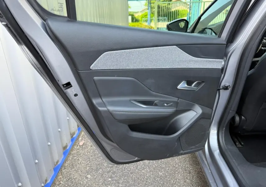 Vue intérieure de la porte arrière gauche d'une Peugeot 308 gris Artense avec garniture noire et tissu gris clair.