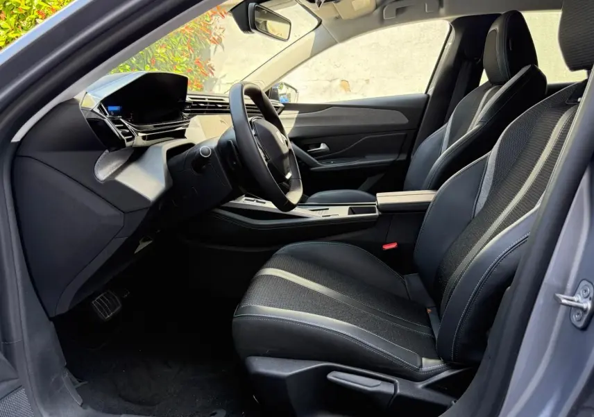 Vue intérieure côté conducteur de la Peugeot 308 2024 gris Artense, avec sièges noirs et tableau de bord moderne.