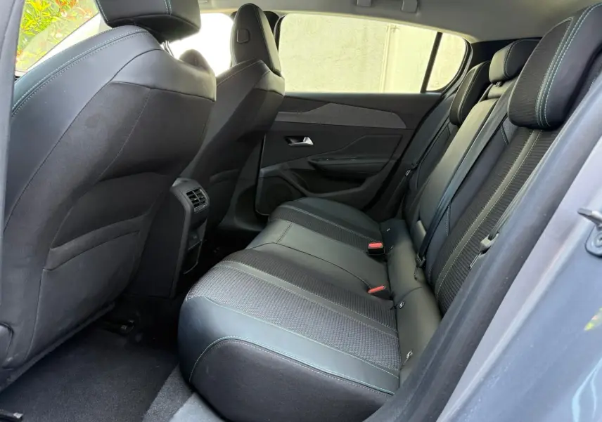 Vue intérieure côté droit des sièges arrière en cuir noir avec surpiqûres vertes d'une Peugeot 308 gris Artense 2024.