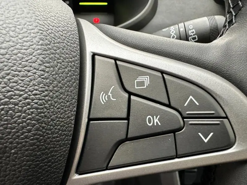 Gros plan sur les commandes multifonctions noires du volant du Dacia Jogger 1.6 hybrid noir nacré, avec bouton OK et flèches directionnelles.