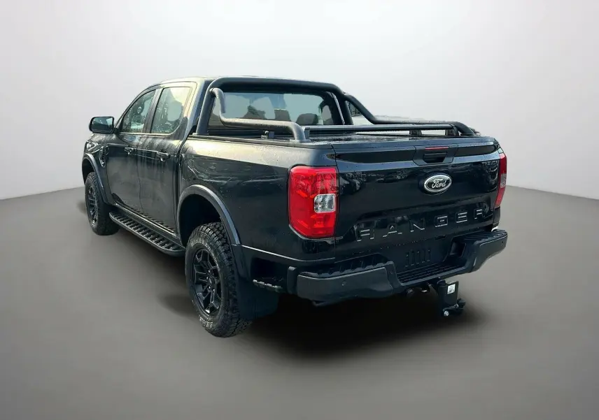 Ford Ranger 2025 noir shadow en 3/4 arrière droit, avec barres de protection et attelage visible sur fond neutre.