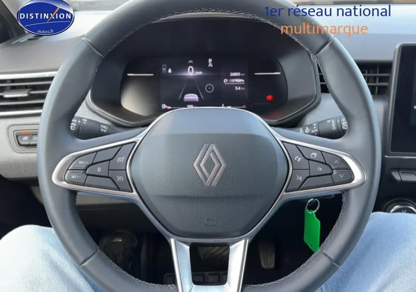 Vue intérieure centrée sur le volant multifonction gris et l'écran numérique du tableau de bord d'une Renault Clio V.