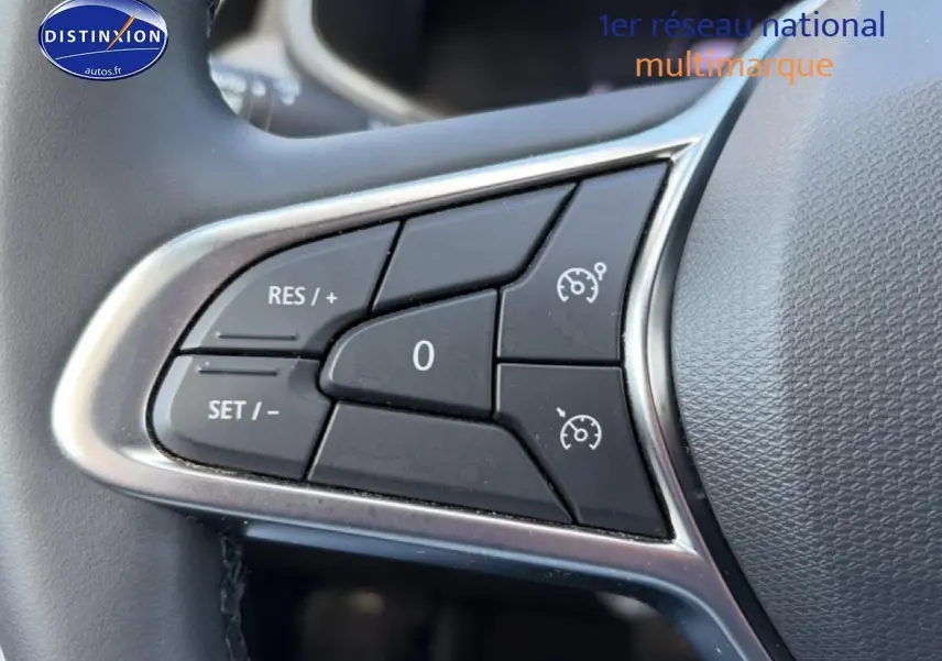 Gros plan sur les commandes noires du régulateur de vitesse au volant gris de la Renault Clio V.