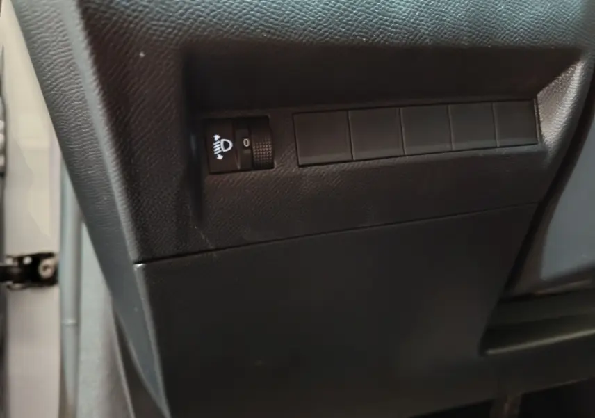 Détail du tableau de bord noir avec molette de réglage des phares dans une Peugeot 208 gris clair côté gauche.