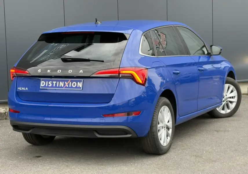 Vue 3/4 arrière droite d'une Skoda Scala 2024 bleu Energy avec feux arrière allumés et jantes alliage argent.