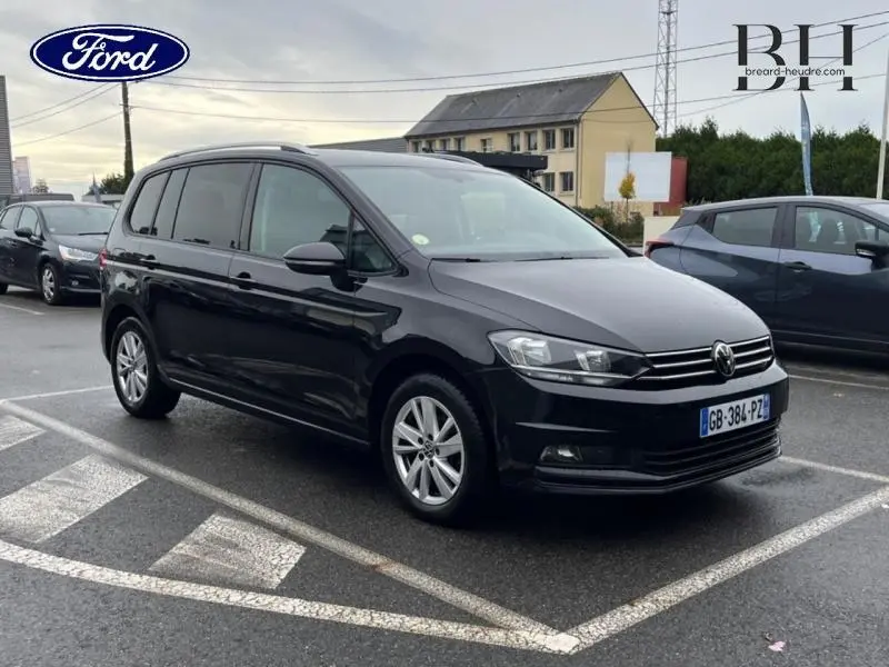Volkswagen Touran noir intense nacré vu de 3/4 avant droit sur parking avec jantes alu et barres de toit.