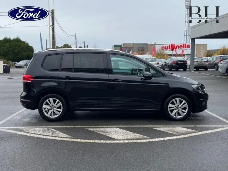 Profil côté droit d'un Volkswagen Touran noir intense nacré stationné sur un parking urbain.