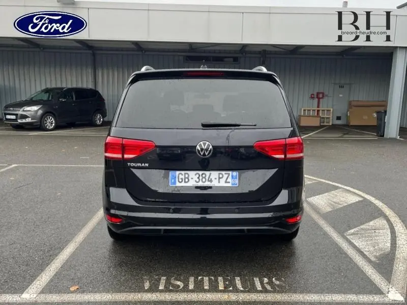 Vue arrière d'un Volkswagen Touran noir intense nacré garé sur une place visiteurs sous un abri.