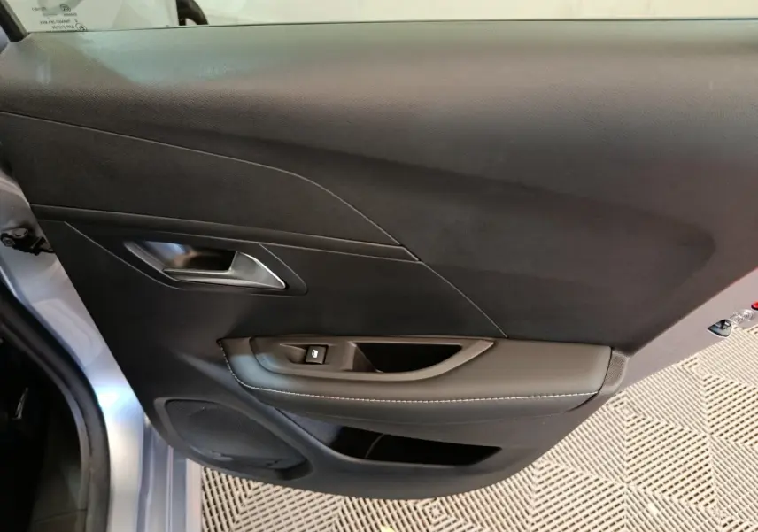 Vue intérieure du panneau de porte côté gauche gris clair d'une Peugeot 208 PureTech 100 S&S Allure avec commande de lève-vitre.