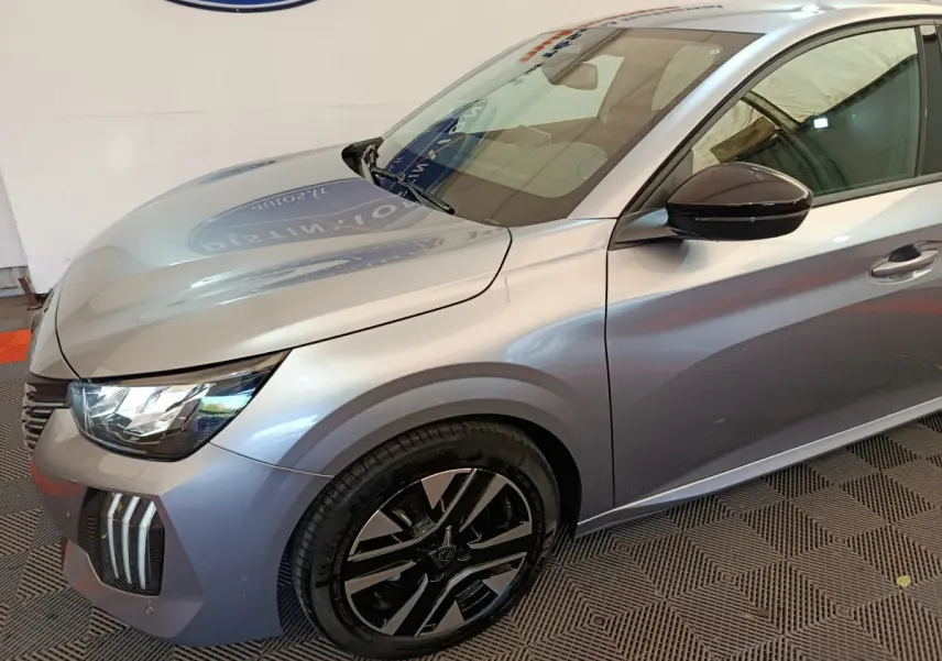 Vue 3/4 avant droite d'une Peugeot 208 gris clair avec jantes noires et rétroviseur droit noir brillant.