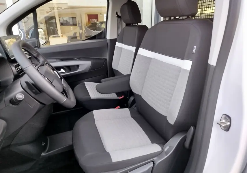 Intérieur avant du Citroën Berlingo 2025 en Kaolin White, sièges tissu gris et noir avec accoudoir central côté droit.