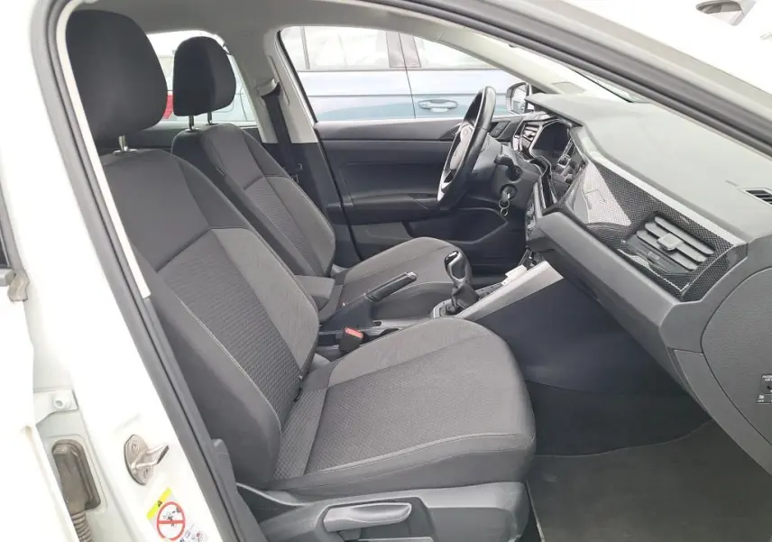 Vue intérieure côté conducteur de la Volkswagen Polo blanche 2023, sièges tissu gris et tableau de bord moderne.