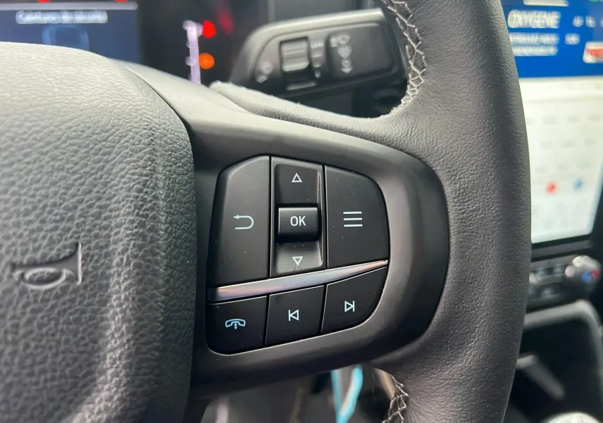 Gros plan sur les commandes au volant du Ford Ranger 2025 bleu lightning, mettant en valeur les boutons multifonctions à droite.