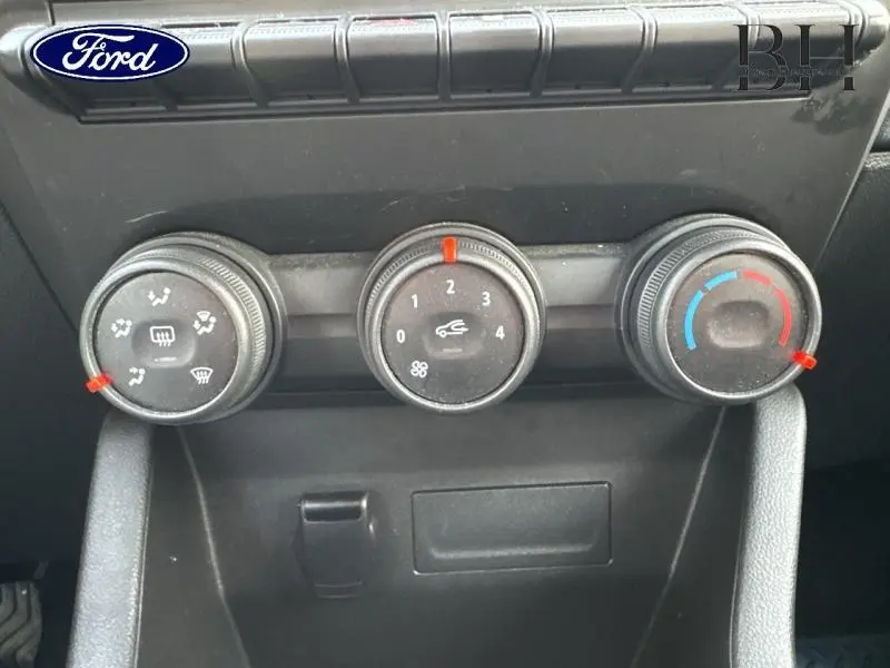 Gros plan sur les commandes de climatisation noires d'une Renault Clio blanche, avec réglages de ventilation et température.