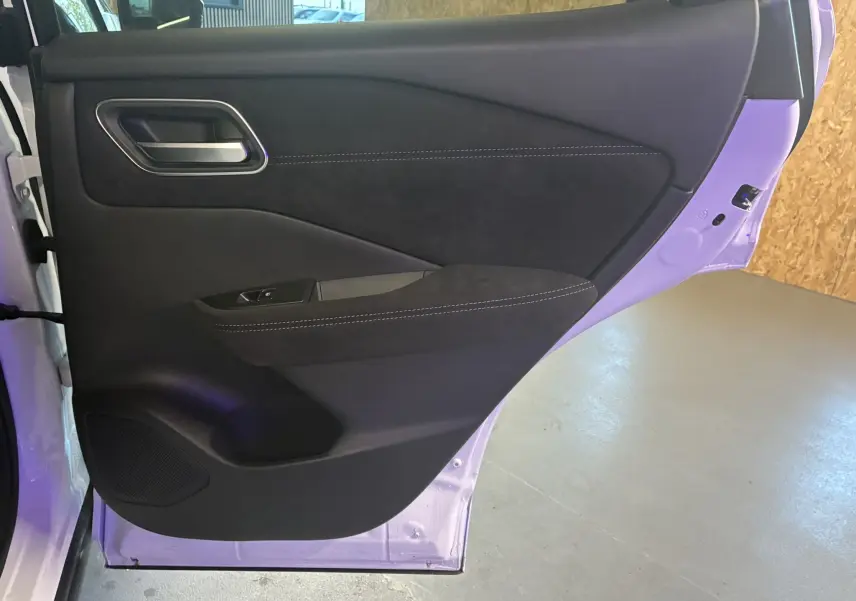 Porte arrière gauche ouverte d'un Nissan Qashqai blanc nacré, intérieur noir avec surpiqûres blanches et poignée métallique.