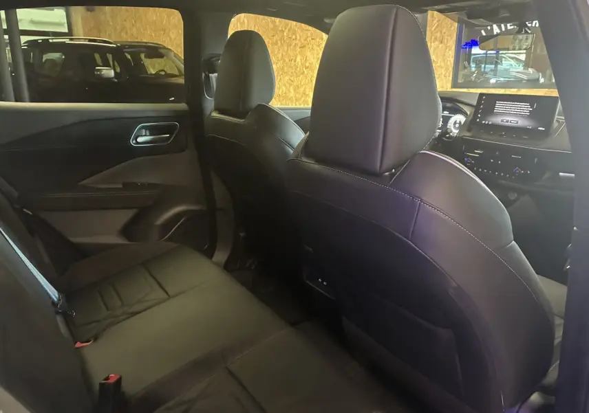 Vue intérieure arrière du Nissan Qashqai 2025, sièges en cuir noir et tableau de bord avec écran tactile visible.