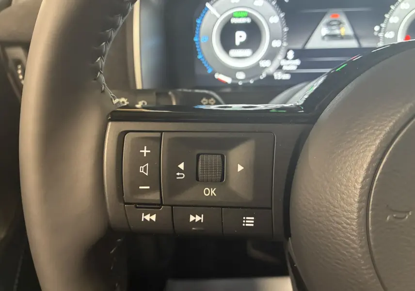 Gros plan sur les commandes gauche du volant noir du Nissan Qashqai 2025 avec tableau de bord numérique en arrière-plan.