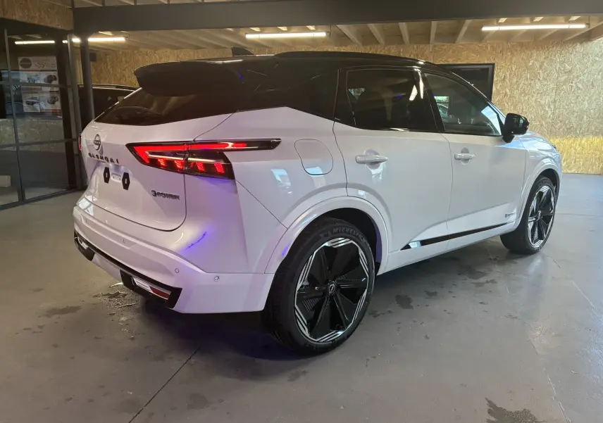 Vue 3/4 arrière droite du Nissan Qashqai blanc nacré avec toit noir et jantes noires distinctives en intérieur showroom.