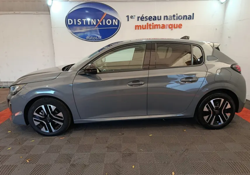 Profil côté gauche d'une Peugeot 208 gris foncé 2025, avec jantes noires et détails modernes visibles en intérieur showroom.