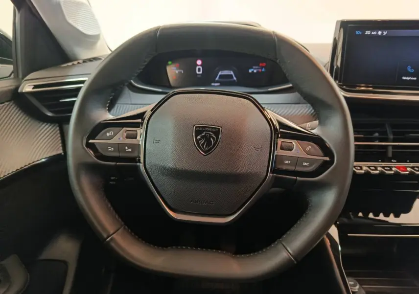Vue rapprochée du volant noir de la Peugeot 208 PureTech 100 S&S Allure 2025 avec tableau de bord digital et écran tactile.