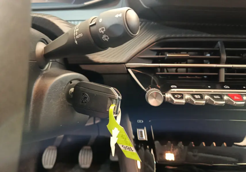 Gros plan intérieur sur le tableau de bord et clé insérée d'une Peugeot 208 gris foncé, avec commandes et ventilation visibles.