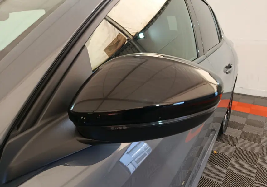 Rétroviseur noir brillant côté conducteur d'une Peugeot 208 gris foncé, vue rapprochée en angle avant gauche.