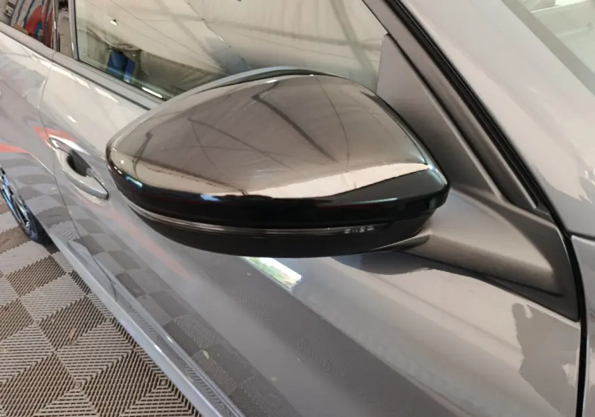 Gros plan sur le rétroviseur droit noir brillant d’une Peugeot 208 gris foncé, vue côté droit.