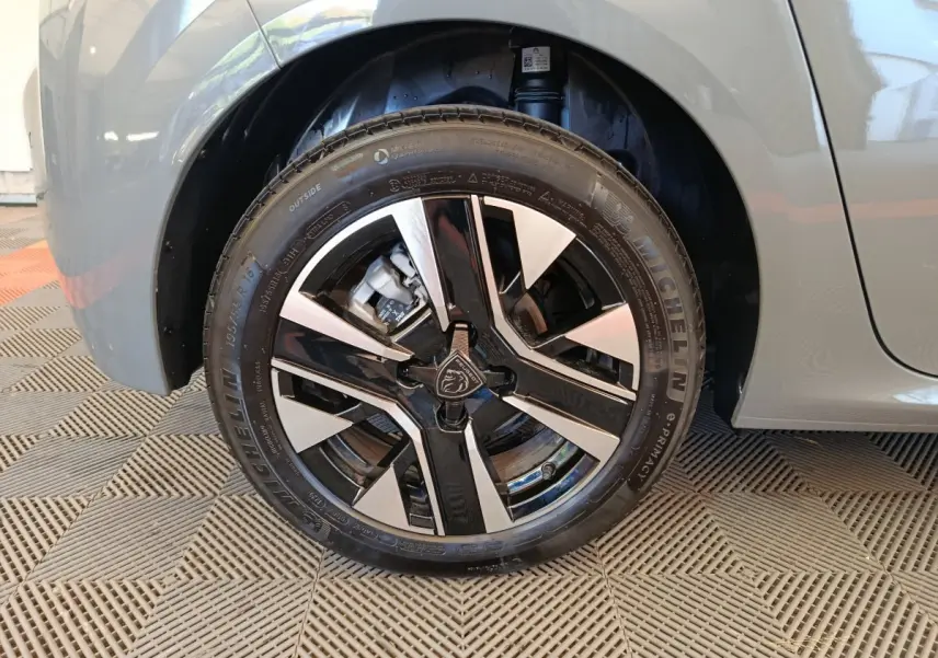 Gros plan sur la roue avant droite de la Peugeot 208 gris foncé, mettant en valeur la jante alliage bicolore au design moderne.