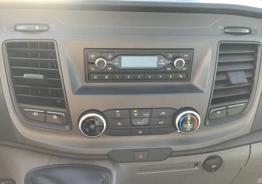 Vue rapprochée du tableau de bord gris du Ford Transit Chassis Cabine blanc, montrant la radio et les commandes de climatisation.