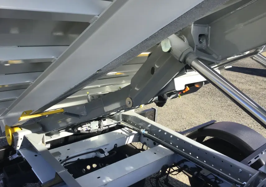 Gros plan sous la benne relevée du Ford Transit Chassis Cabine blanc, montrant le bras de levage et le châssis métallique.