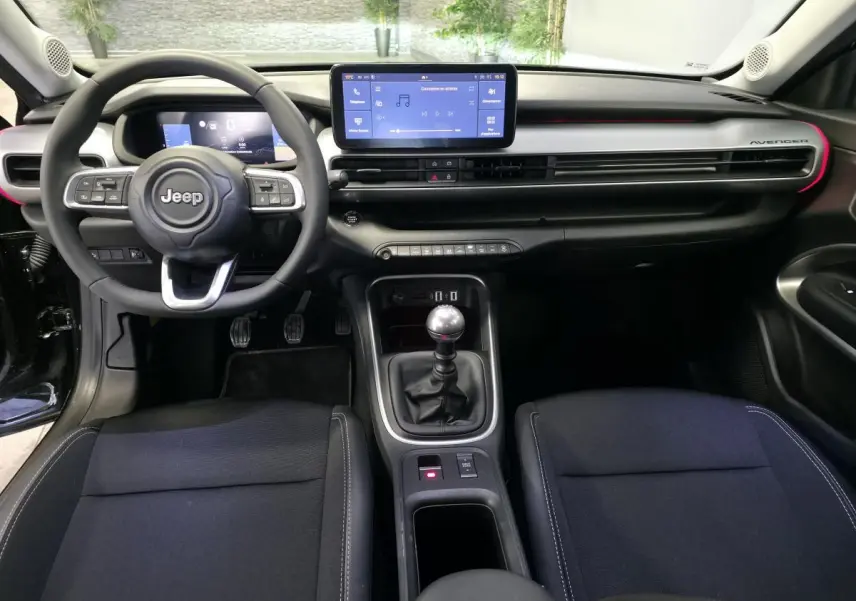 Vue intérieure avant du Jeep Avenger noir 2025, tableau de bord moderne avec écran tactile et levier de vitesses manuel.