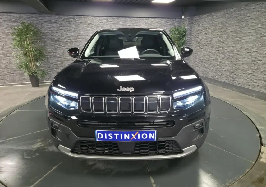 Vue avant d'un Jeep Avenger noir 2025 avec calandre gloss black et phares LED allumés en intérieur showroom.