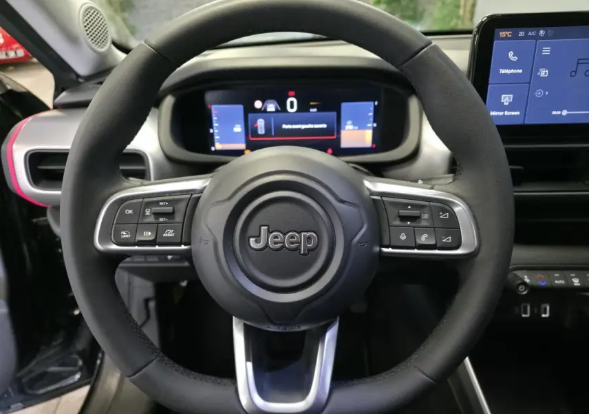 Vue rapprochée du volant noir Jeep Avenger 2025 avec commandes intégrées et tableau de bord numérique en arrière-plan.