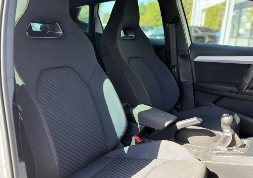 Vue intérieure côté conducteur de la SEAT Ibiza TSI 115 FR 2025, sièges sport noirs avec surpiqûres rouges et levier de vitesse manuel.